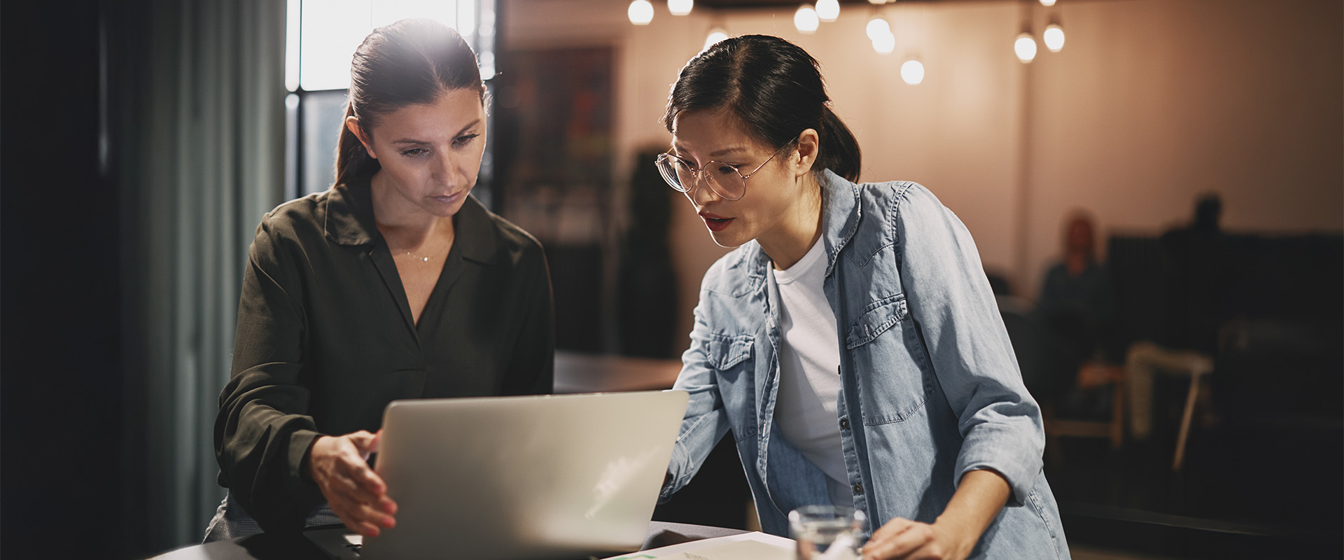 zwei Frauen schauen auf einen Laptop und sprechen miteinander